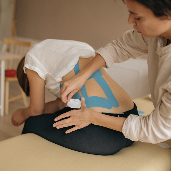 Physiotherapist applies kinesiology tape to injured lower back of patient on massage table