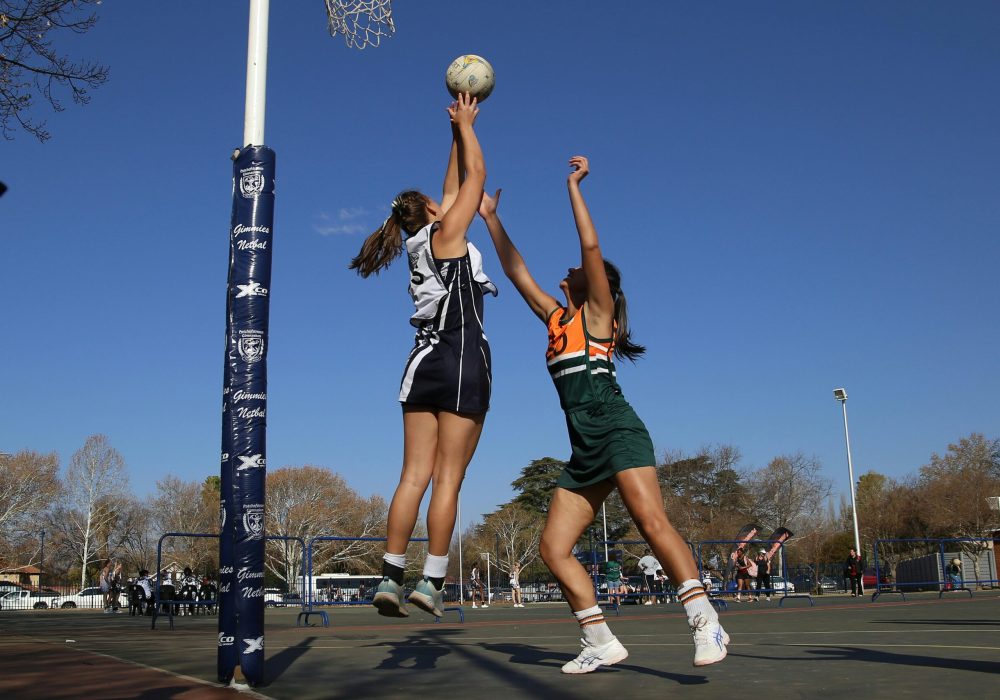 Two female netball players in action on an outdoor court during a sunny day.